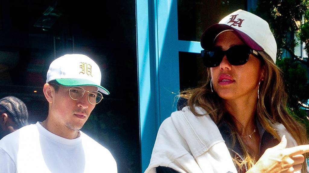 Spotted checking out of their Tribeca hotel, Jessica Alba and boyfriend Danny Ramirez exuded casual-cool energy in perfectly coordinated streetwear. Alba paired a sporty windbreaker with a draped cream sweater, white joggers, a chic quilted crossbody bag, an LA baseball cap and Gucci sunglasses for an understated yet polished look. Ramirez complemented her style with a crisp white tee, denim, and a matching baseball cap, both clutching bottles of sparkling water for their stroll.  Pictured: jessica alba,danny ramirez
